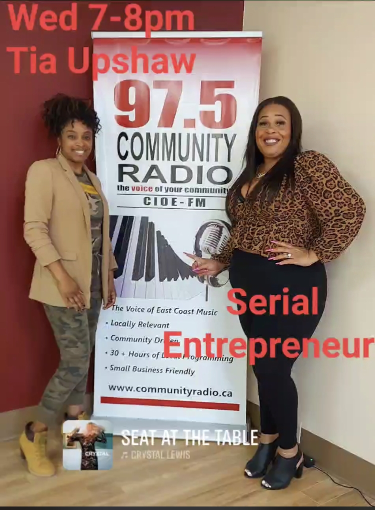 Two Black ladies pose in front af a radio station promotional poster