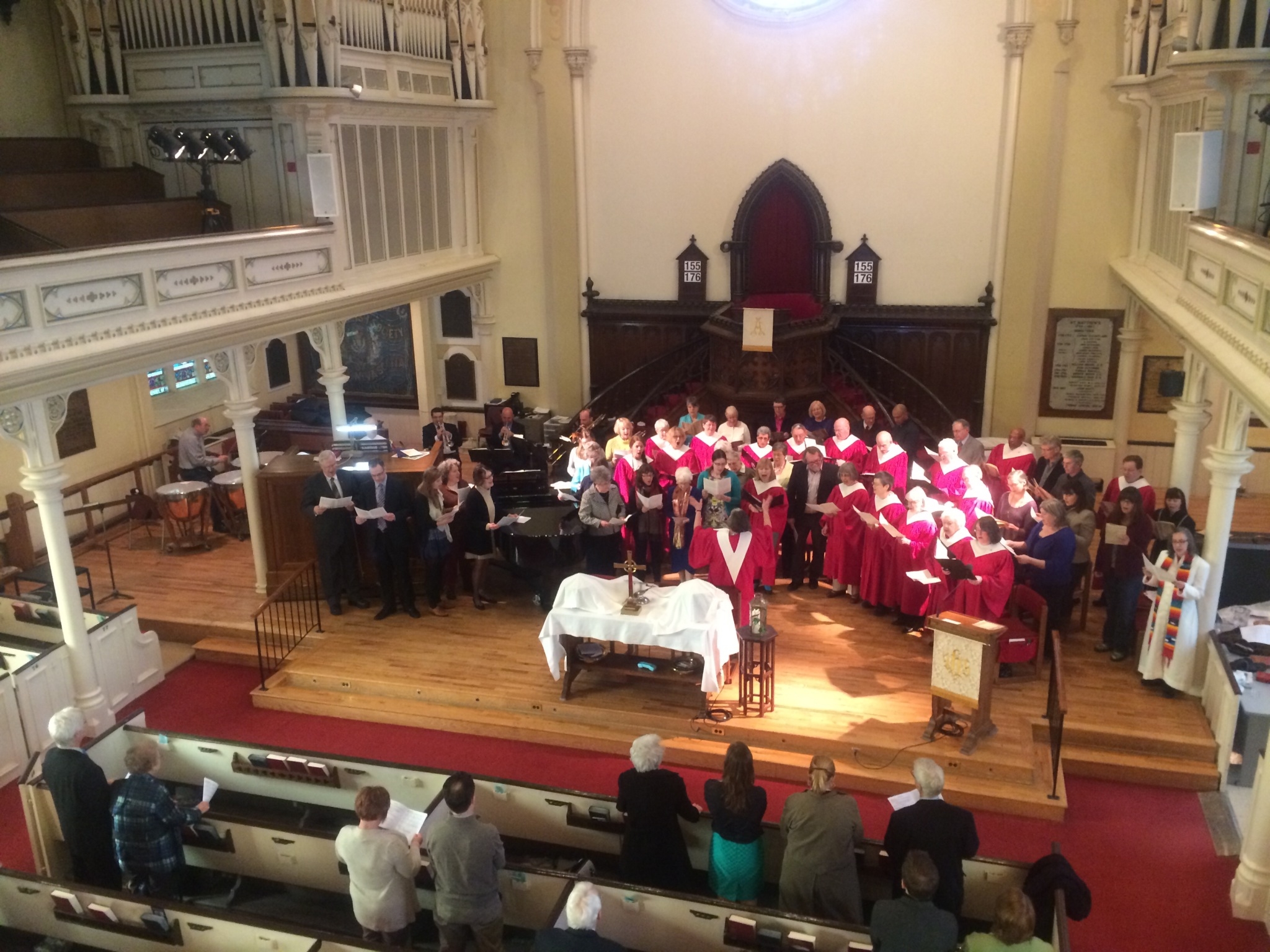 A look down into a church sanctuary with a choir in red robes singing while the congregation sits in the pews.