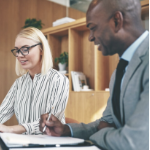 一个年轻的白人妇女和一个黑人男子坐在办公室的会议桌旁