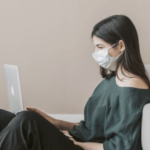 一个戴着面具的白人少女在用她的笔记本电脑