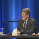 一个年长的白人拿着麦克风坐在桌子旁