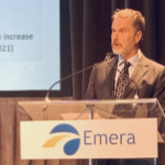 一个年长的白人在讲台上讲话，上面有标志阅读Emera