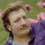 一个年轻的白人，有红头发和胡须，在粉红色的塑料火烈鸟田里