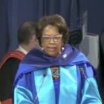 一个穿着明亮蓝色缎面长袍的黑人妇女在讲台上说话