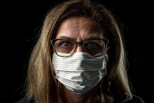 一位深金色头发、戴着黑框眼镜的妇女戴着白色带蓝色横条的面具。黑屏的背景。