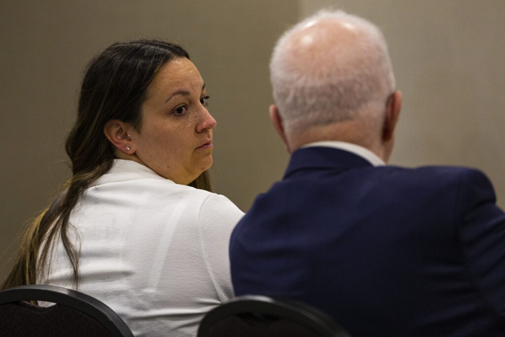 一个穿白衬衫的女人从她的右肩上望过来一个穿蓝色西装的白发男人。他们在一间米色的房间里，坐在不舒服的椅子上。