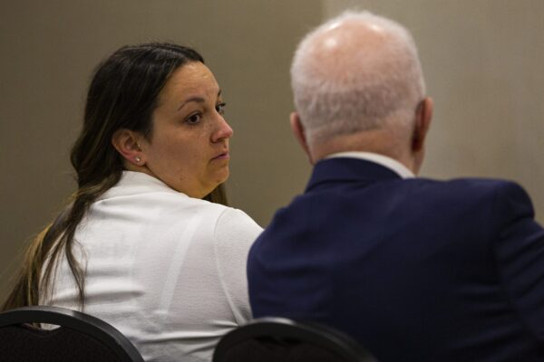 一个穿白衬衫的女人从她的右肩上看过去，一个穿蓝色西装、头发花白的男人。他们在一个米色房间里，坐在不舒服的椅子上。