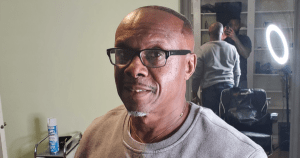 一名戴着黑色眼镜、穿着灰色毛衣的黑人对着镜头微笑