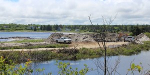 一处建筑工地，一辆白色卡车停在一堆土附近。场地被水环绕