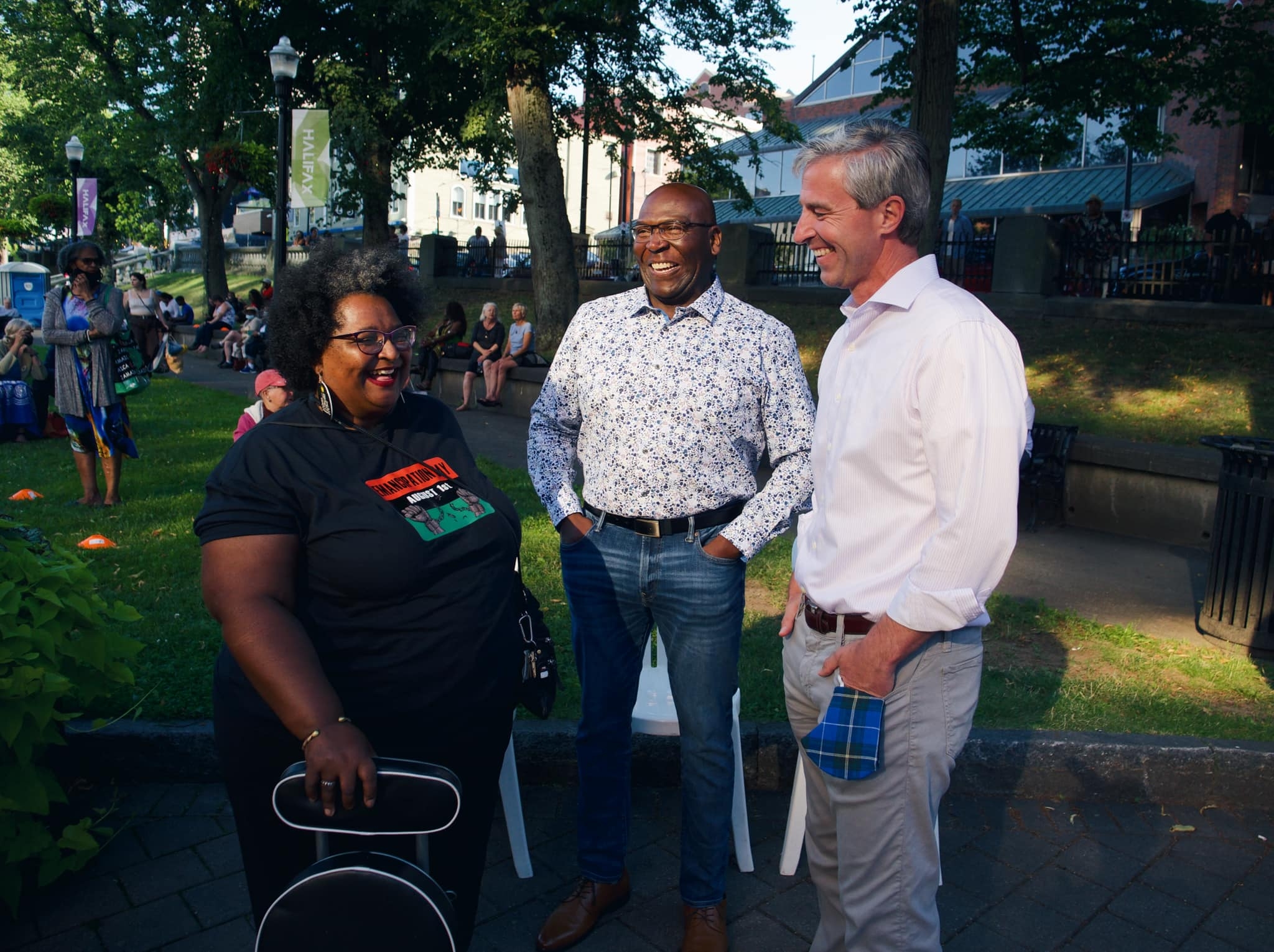 一个女人和两个男人站在公园里，三个人都在笑。