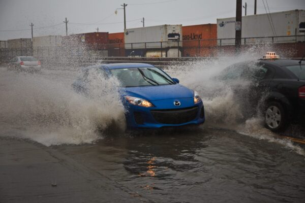 一辆蓝色的汽车在黑暗的日子里引起了很大的轰动。从蓝色汽车流出的水浸湿了一辆向相反方向行驶的出租车的挡风玻璃。在这些车辆的后面是与道路平行的火车轨道上的一系列集装箱。
