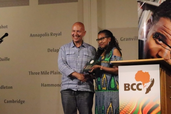 A Black woman presents an award to a Black man at a podium.