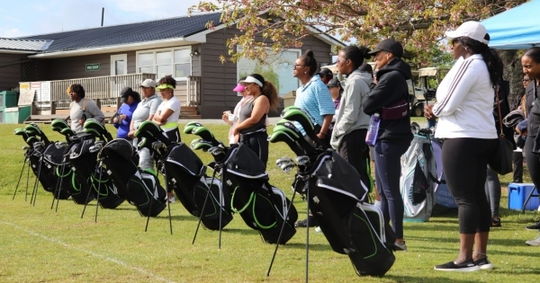 一群妇女连续站在一起。每个女人都站在高尔夫球袋前，听着关于打高尔夫球的技巧。