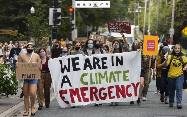一群人在一次集会中沿着街道游行，同时举着一个牌子，上面写着我们正处于气候紧急状态