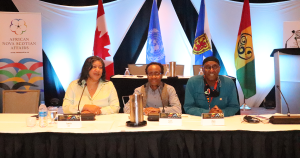 背景是加拿大国旗，联合国国旗，新斯科舍省国旗，非洲新斯科舍省国旗，三名黑人新斯科舍省人坐在桌子上进行小组讨论。