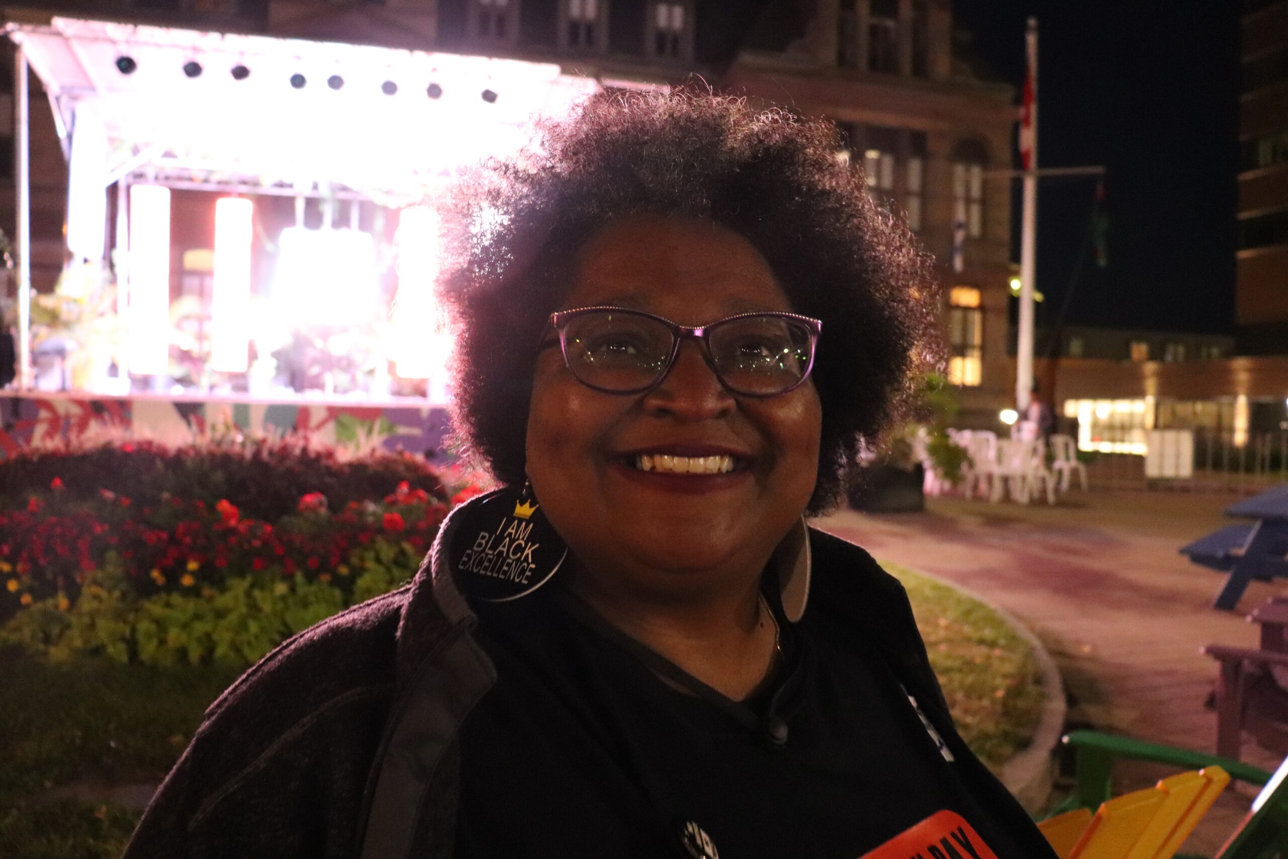 夜间特写镜头的黑人女士与爆炸头和眼镜微笑与舞台灯光在背景。