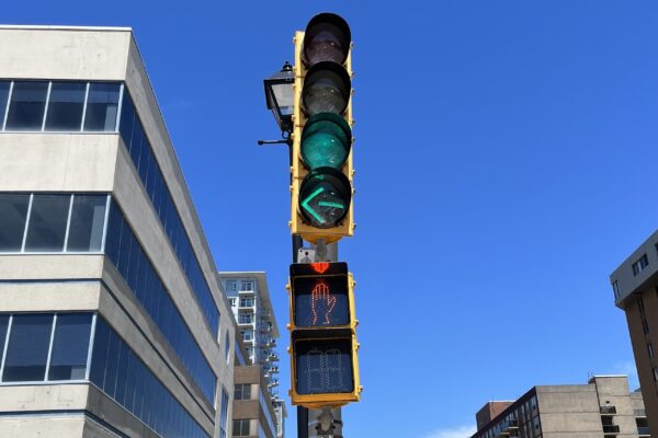 在阳光明媚的日子里，从低角度看红绿灯。交通方面，有一个普通的绿灯和一个绿色的左转信号。对于行人，有一只橙色的手。在街道的两边可以看到一些建筑物。