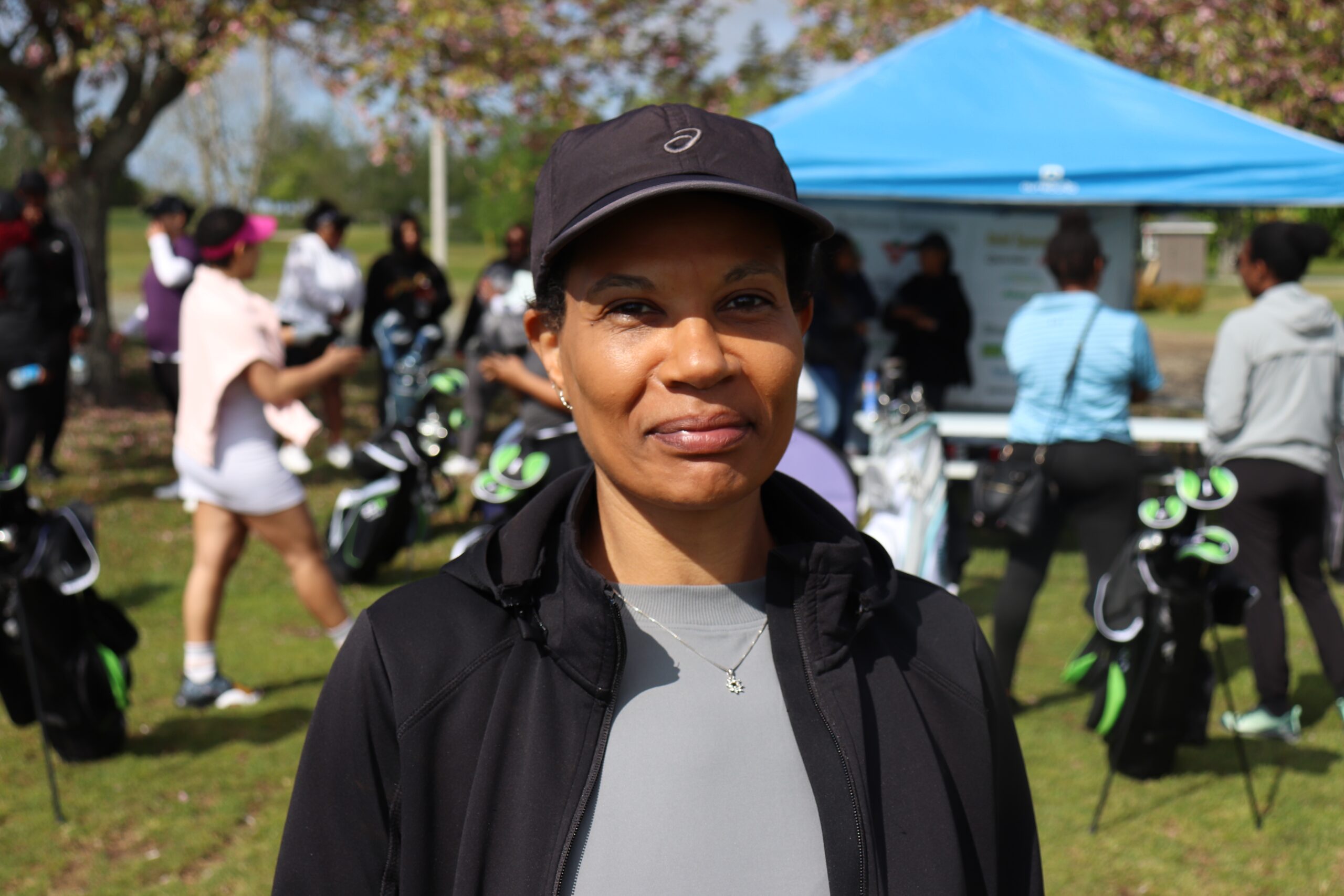 Black lady in dark baseball cap and black zip-up jacket, and grey shirt