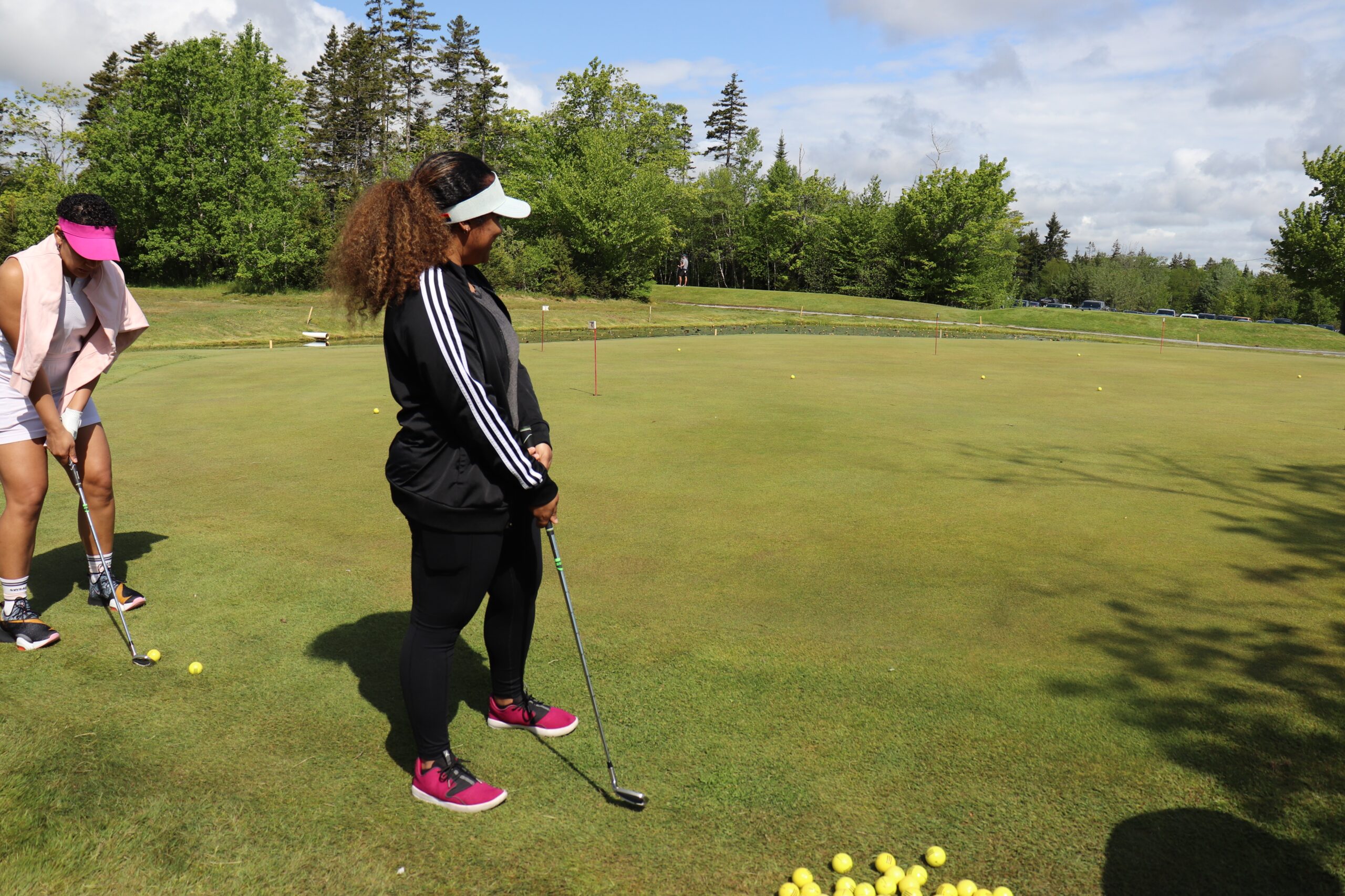 黑色裤子和黑色外套的黑人妇女将球放在高尔夫绿色上后看着她的球