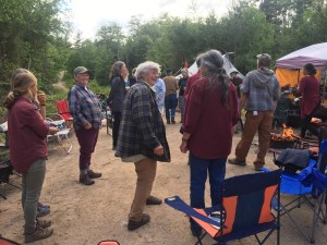 在一个被树木环绕的露天营地，十几个人站在篝火旁。他们面带微笑，天气阴沉得令人愉快。