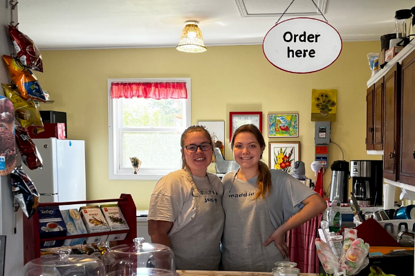 两名年轻女子站在一家咖啡馆的柜台后面。上面有个牌子写着“此处秩序井然”。