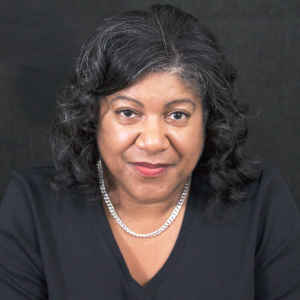 一个带有友善笑容的黑人妇女，穿着黑色V脖子毛衣和大胆的银色链接项链