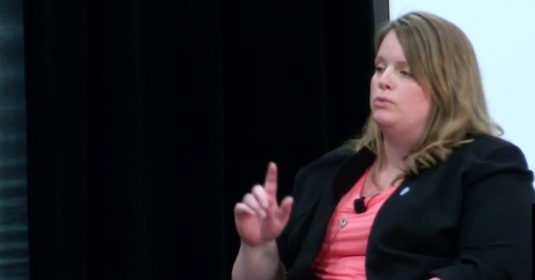 一个穿粉色衬衫的女人，坐着，举起食指