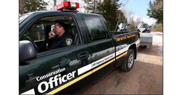 一名身穿制服的环保官员驾驶着一辆深绿色的皮卡，皮卡上饰有白色和黄色条纹，并印有“环保官员”字样。