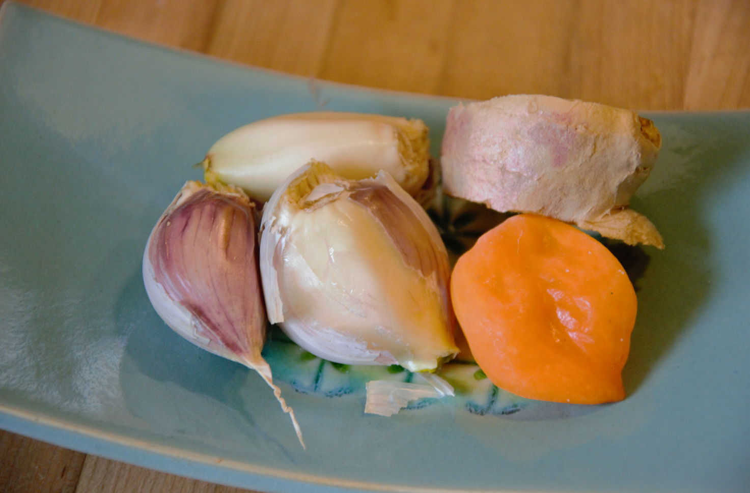 一种陶瓷碟，里面有几瓣大蒜，一片生姜和一根苏格兰胡椒。