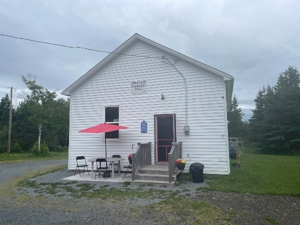 一座白色的单层老建筑，坐落在一块有绿色草坪的平地上。楼外有一张桌子、几把椅子，头顶上有一把红伞。