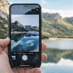 一个白人的手拿着手机，他们正在给一个可爱的湖拍照