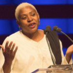 一位留着金色短发的黑人妇女在讲台上讲话