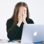 一名年轻女子在笔记本电脑面前，双手疲惫不堪