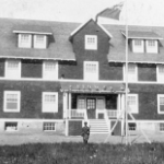 An old photo of a dark shingled three storey building with white trim