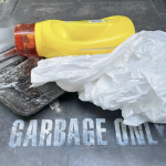 A yellow plastic detergent bottle and a plastic grocery bag on top of a garbage can