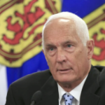 一名身穿西装、一头白发的白人男子在挂满新斯科舍省国旗的墙前讲话