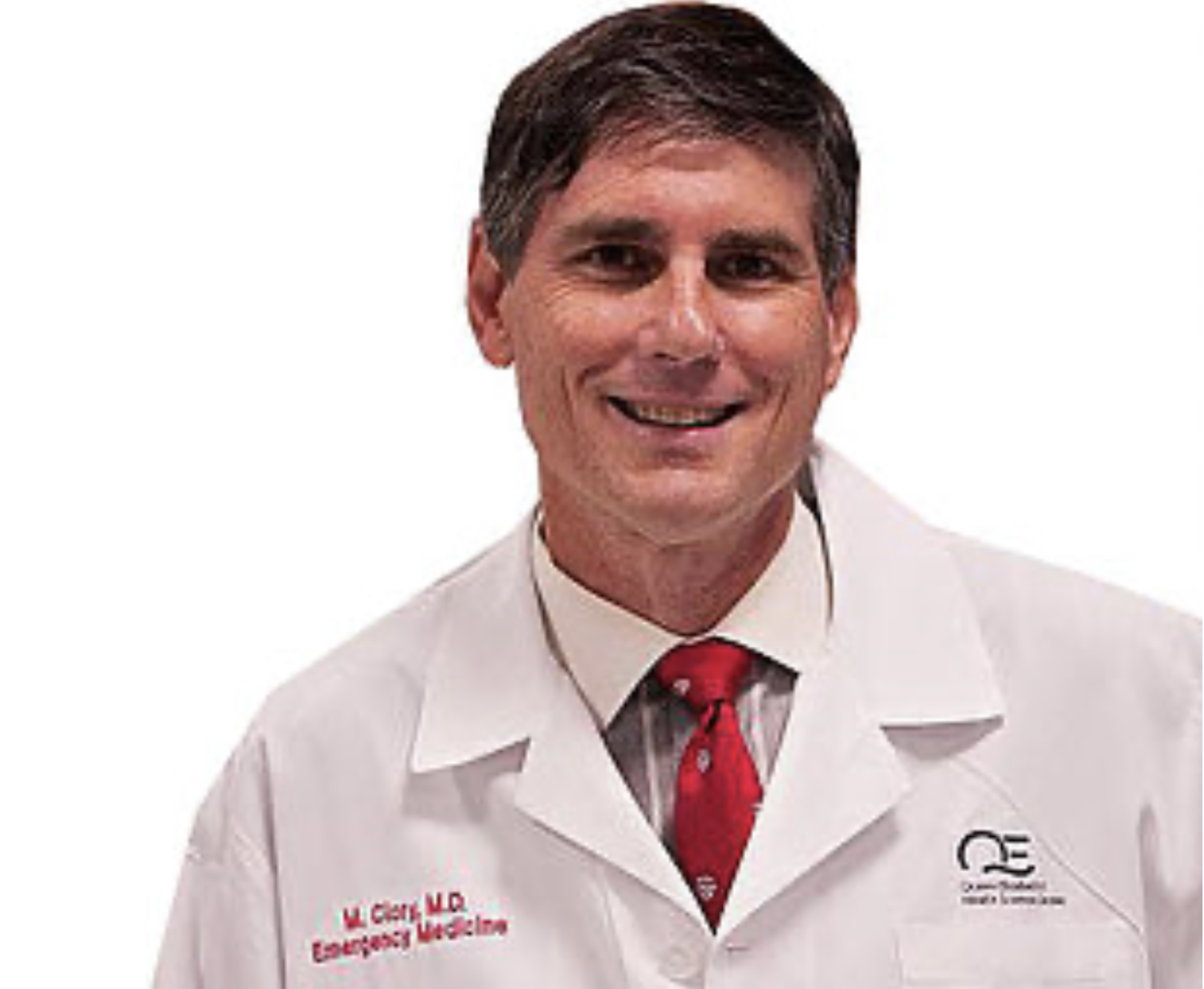一名深色头发的男医生，身穿白衬衫，系着红领带，白色实验室大褂上印有红色浮雕字母，显示他从事急诊医学工作。