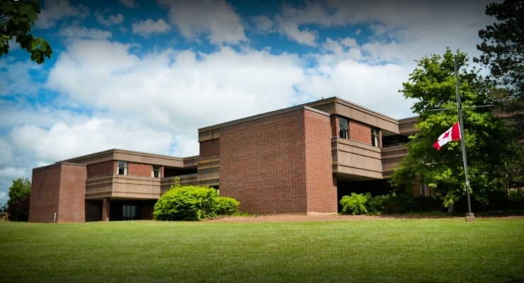 一栋红砖建筑坐在蓝色和多云的天空下的倾斜绿色草坪上。加拿大国旗飞出前面