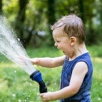 一个穿着蓝色T恤的小男孩在外面玩花园软管