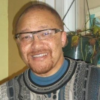 Headshot of Black man in Black glasses and sweater smiling
