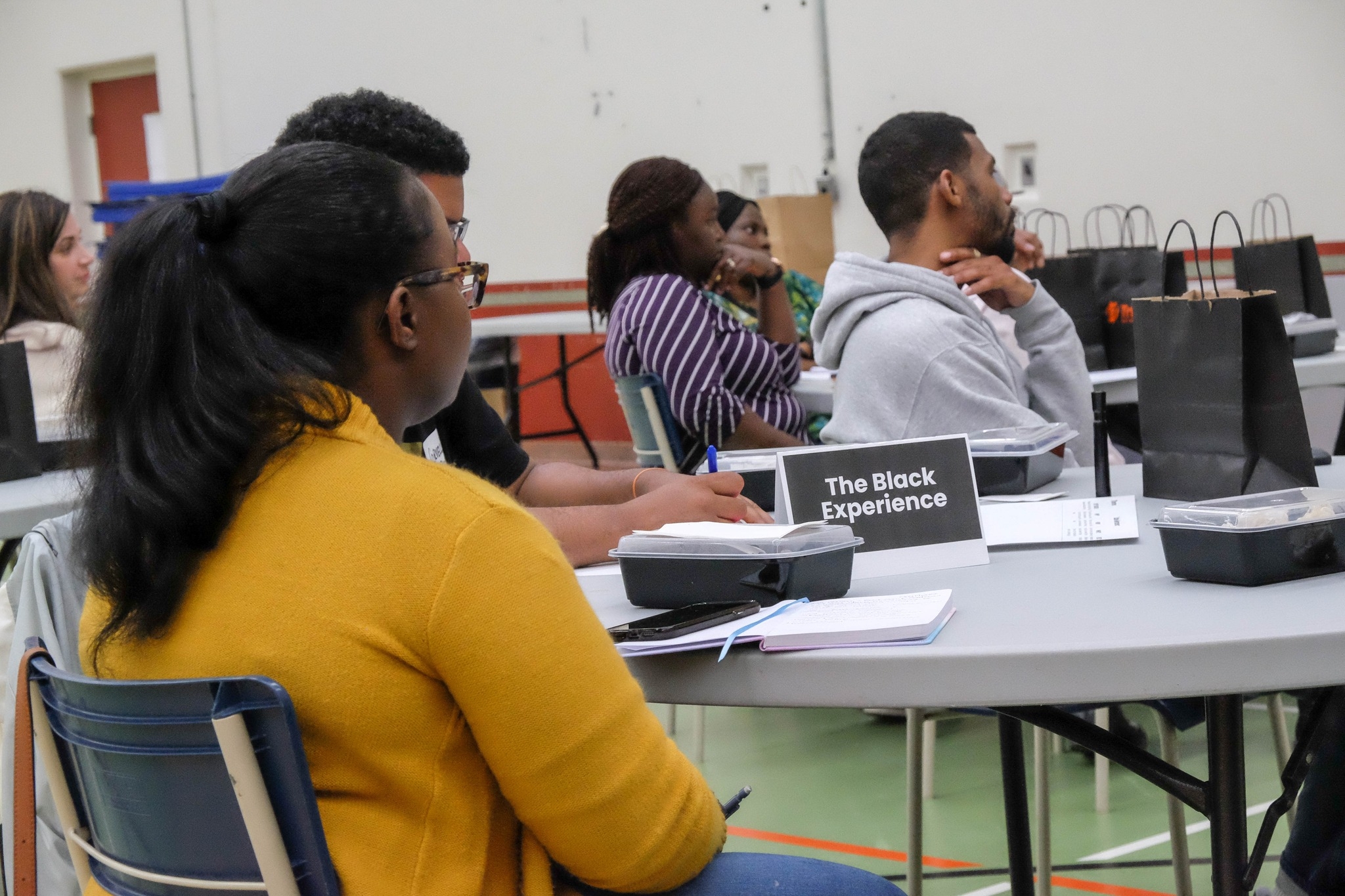 人们在听演讲时坐在桌子旁。在其中一张桌子上是一个标语，上面写着“黑人体验”。