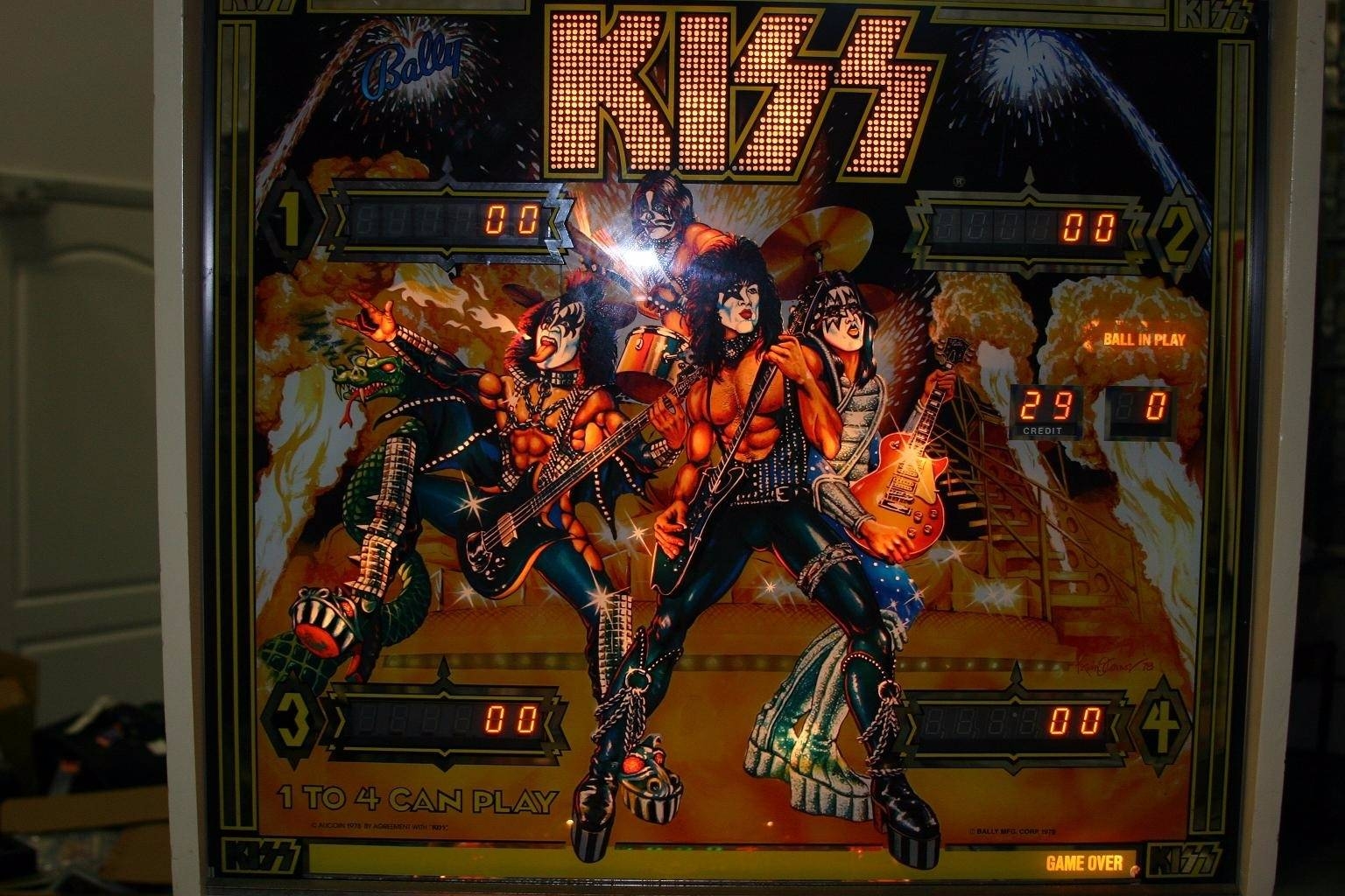 KISS弹球机的后玻璃，灯光下的字母KISS，乐队成员穿着古怪的舞台服装。紧身裤，厚底鞋，化妆。