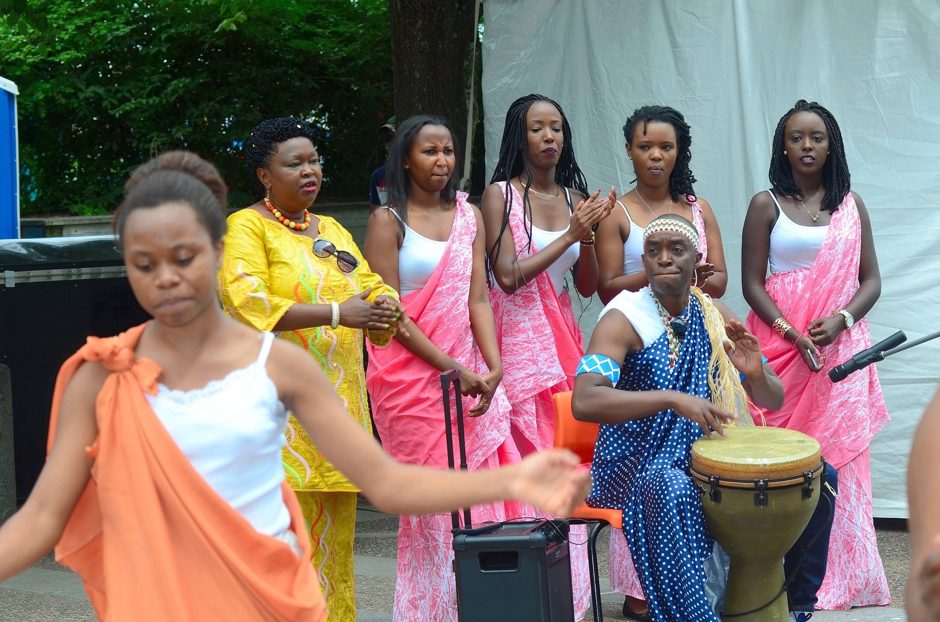 一群穿着彩色外衣和长袍的妇女在一个打鼓的男人后面跳舞鼓掌。