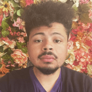 安德烈·芬顿(Andre Fenton)，一个留着小胡子和山羊胡的年轻黑人，背景是玫瑰和其他粉红色的花朵