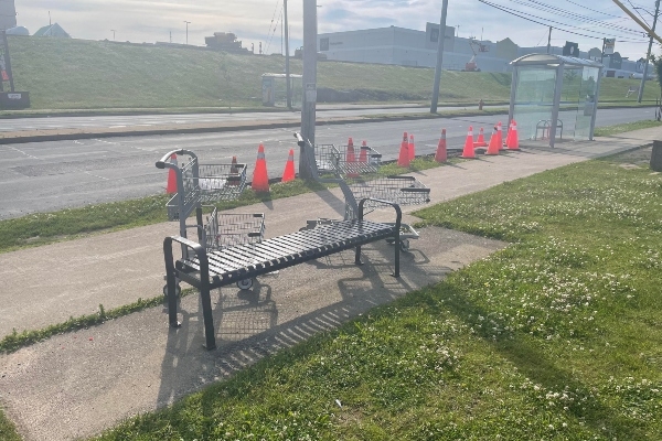 公交车站附近的长凳旁放着两辆购物车。背景是公共汽车候车亭旁边一排橙色的电塔。