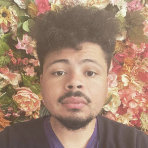 安德烈·芬顿(Andre Fenton)，一个留着小胡子和山羊胡的年轻黑人，背景是玫瑰和其他粉红色的花朵