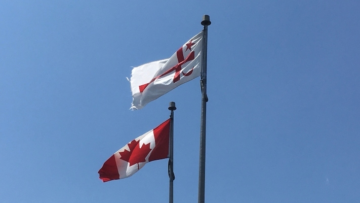 Two red and white flags flying under a blue sky