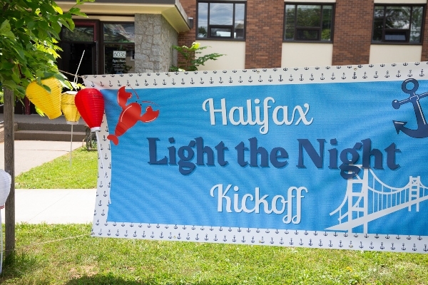 两棵树之间悬挂着蓝色的横幅。横幅读取Halifax Light在夜间开球。