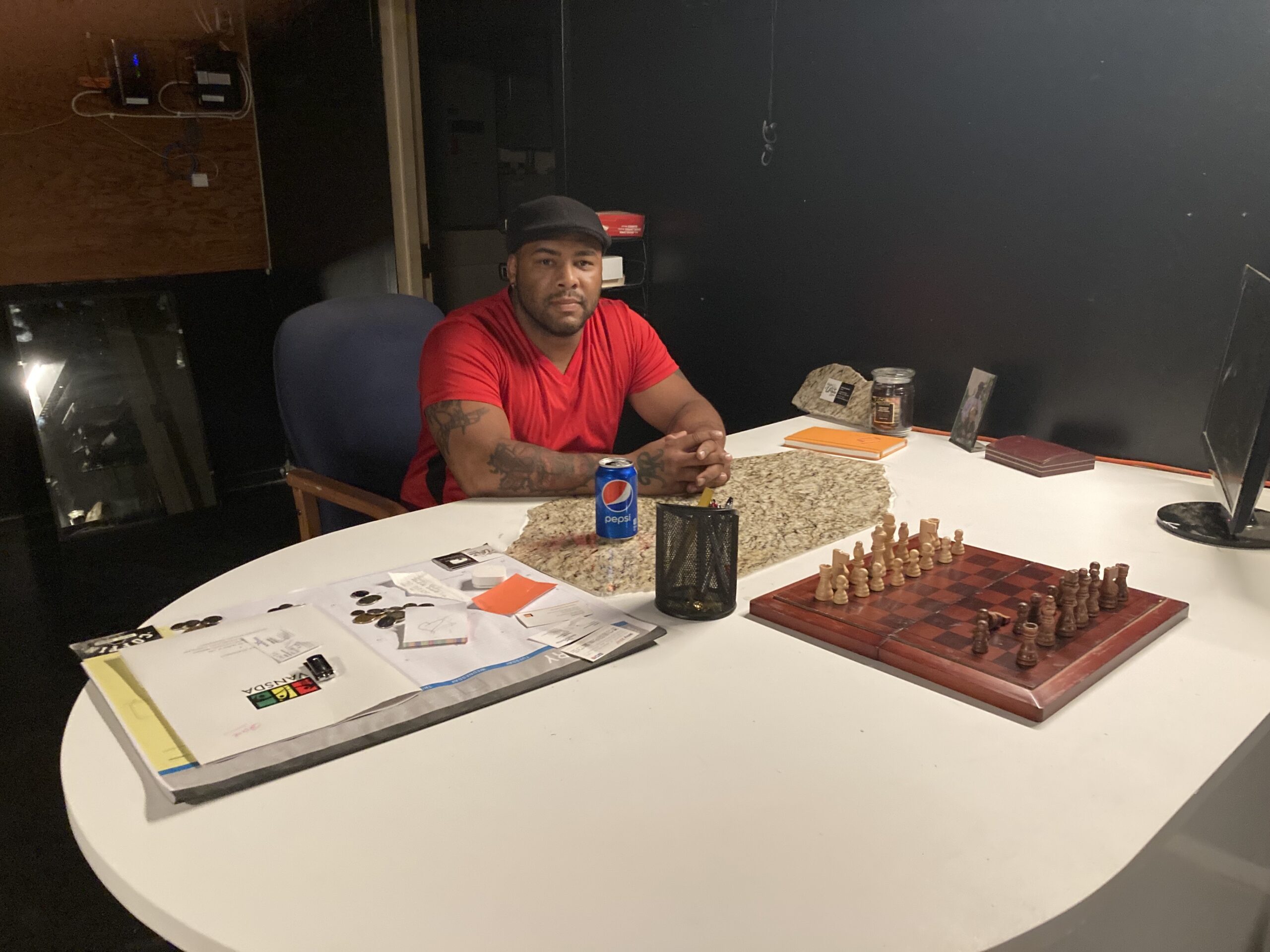 黑人穿着红色T恤和黑色帽子坐在桌子上