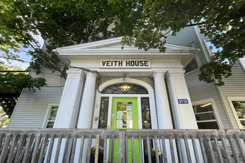 房子的正面有垂下的树叶。这是一座古老的建筑，入口处有两根柱子和一扇绿色的门。门的上方写着“VEITH HOUSE”。